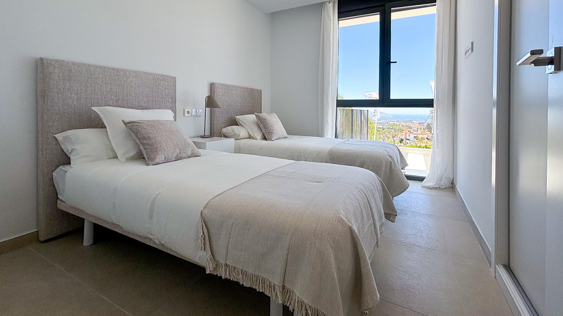 Twin beds in a bright hotel room with a large window revealing a sea view outside.