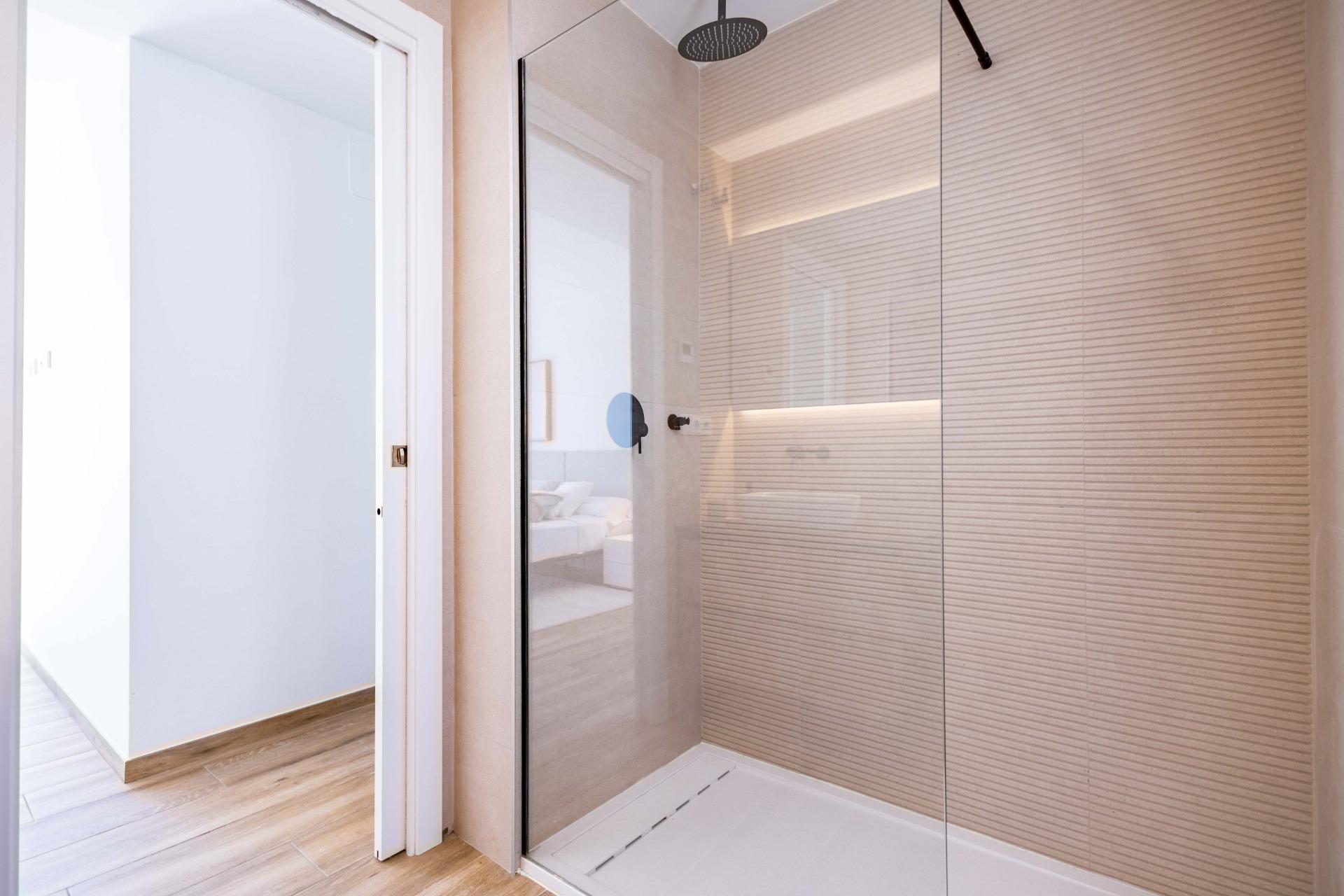 Modern glass-walled shower with a large round rain shower head and beige textured tile walls in a contemporary bathroom.