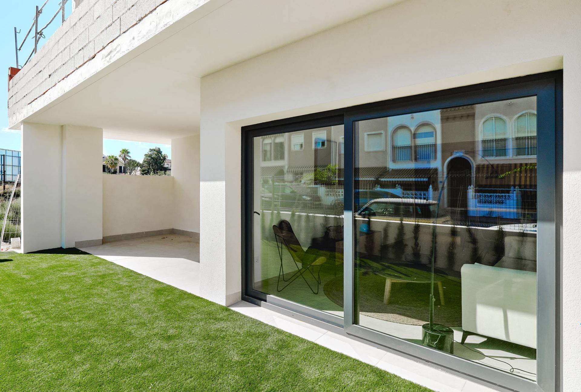 Modern white house exterior with a large glass sliding door, black frame, and a well-kept green lawn; reflections show neighboring homes.
