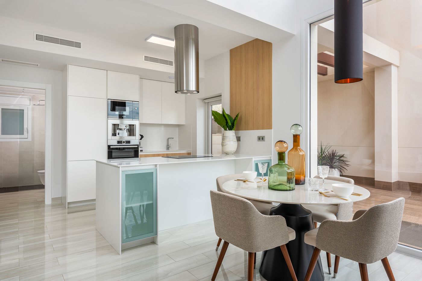Bright, open-concept kitchen and dining area with white cabinets, a glass-front island, and a round table set for four near a large window.
