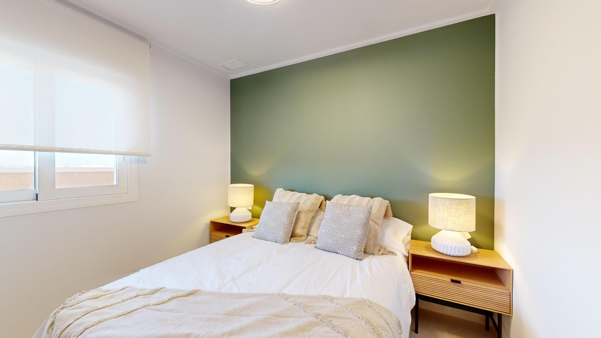 Bedroom with a green feature wall behind a bed, two wooden nightstands, and matching lamps.]','