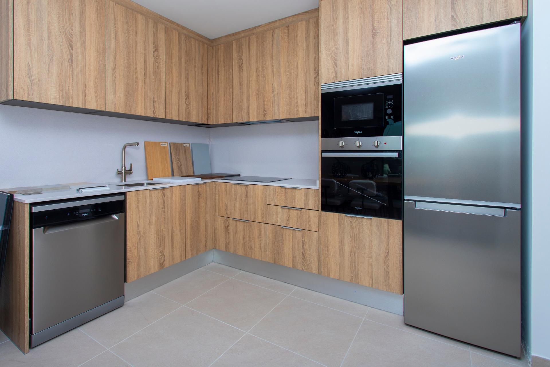 Corner kitchen with oak veneer cabinets, a stainless steel fridge, built-in oven and microwave, and light gray countertops.