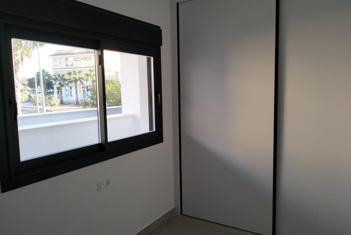 Modern interior: window with a black frame, view of street and palm trees, beside a large white wardrobe with sliding doors