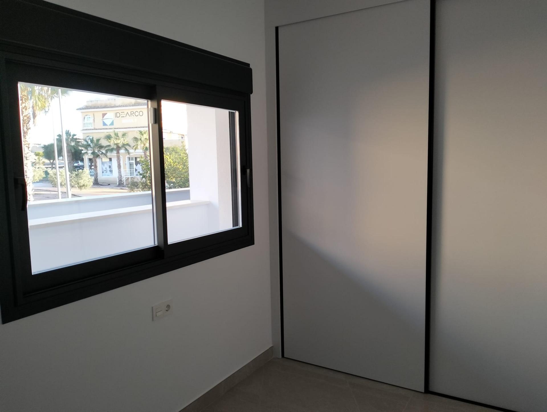 Modern interior: window with a black frame, view of street and palm trees, beside a large white wardrobe with sliding doors