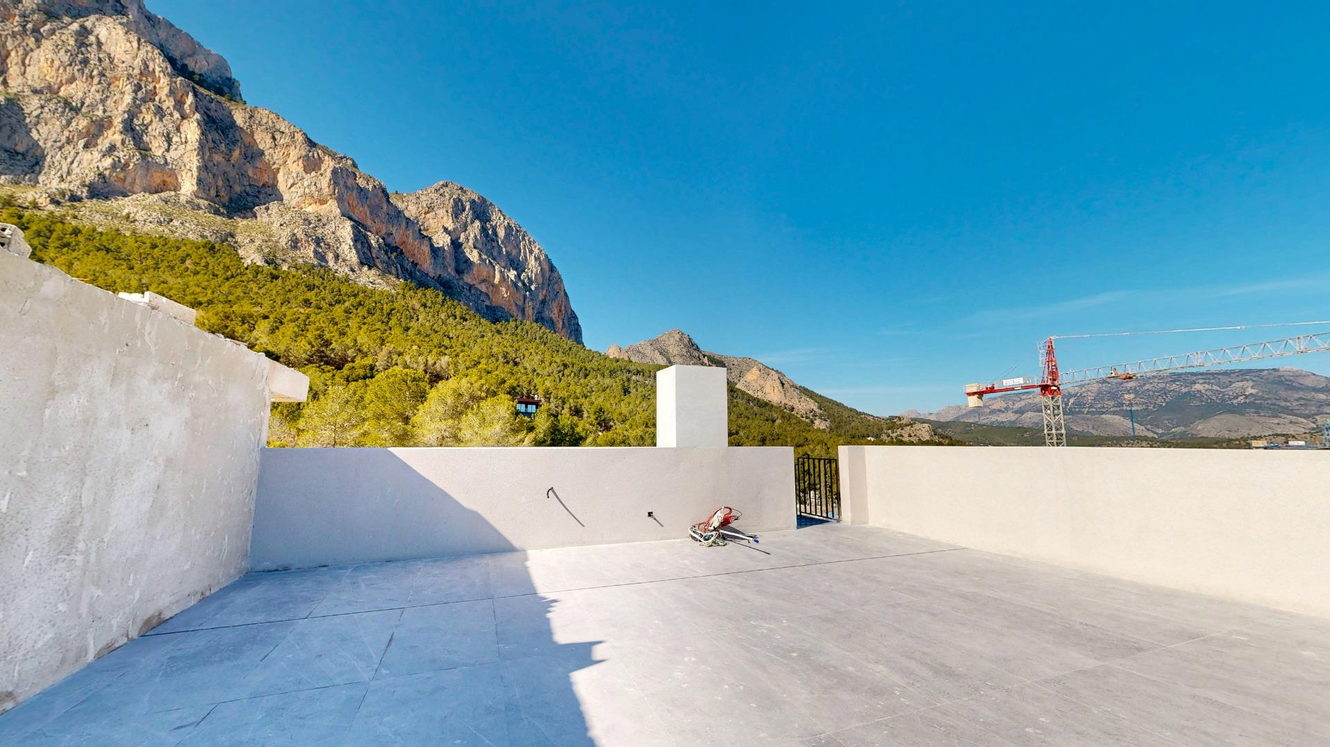 Open concrete terrace with white walls, mountains and a crane in the distance under a clear blue sky.