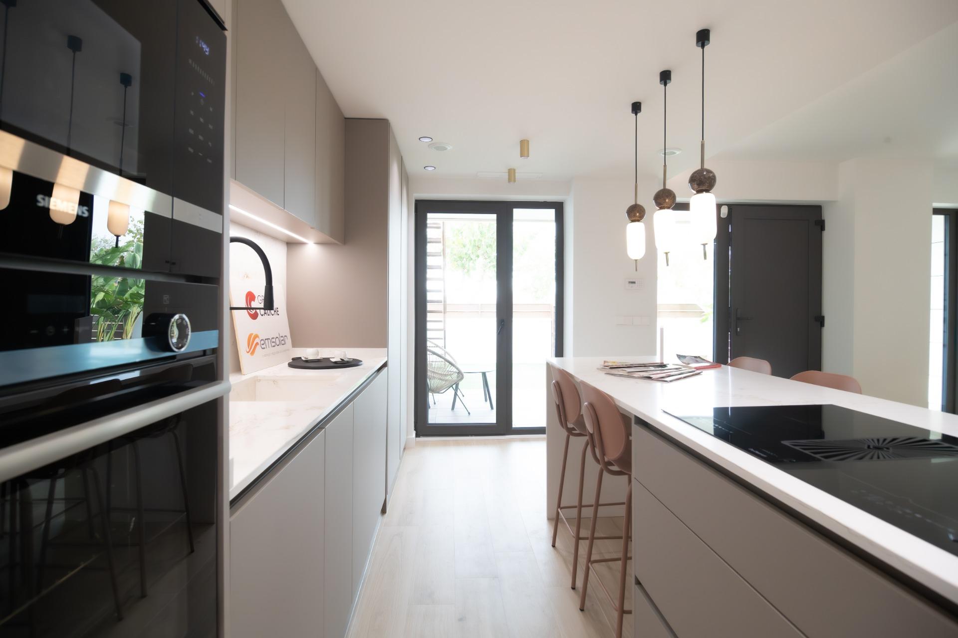 Modern kitchen with gray cabinetry, a white countertop island, and hanging pendant lights; glass door leads to an outside patio.
