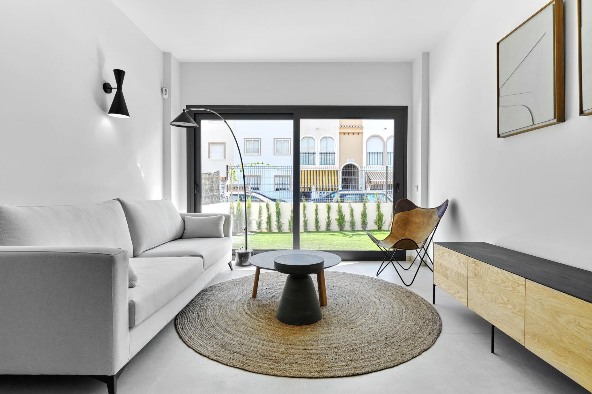 Modern living room with a gray sofa, round jute rug, and large glass sliding doors to an outdoor area.