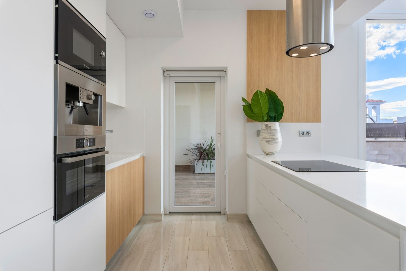 Modern white kitchen with built-in oven and microwave, wooden lower cabinets, and an island with a glass induction cooktop.