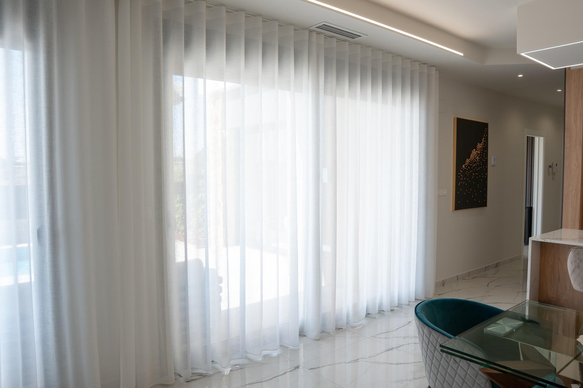 Bright modern living area with floor-to-ceiling sheer white curtains along a large window, marble floor, and contemporary furniture.