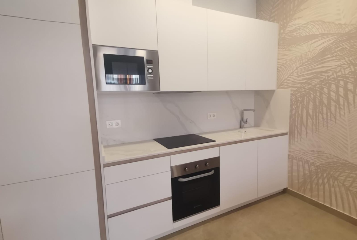 Modern white kitchen with built-in microwave, oven, and induction cooktop, plus a marble backsplash and sink.