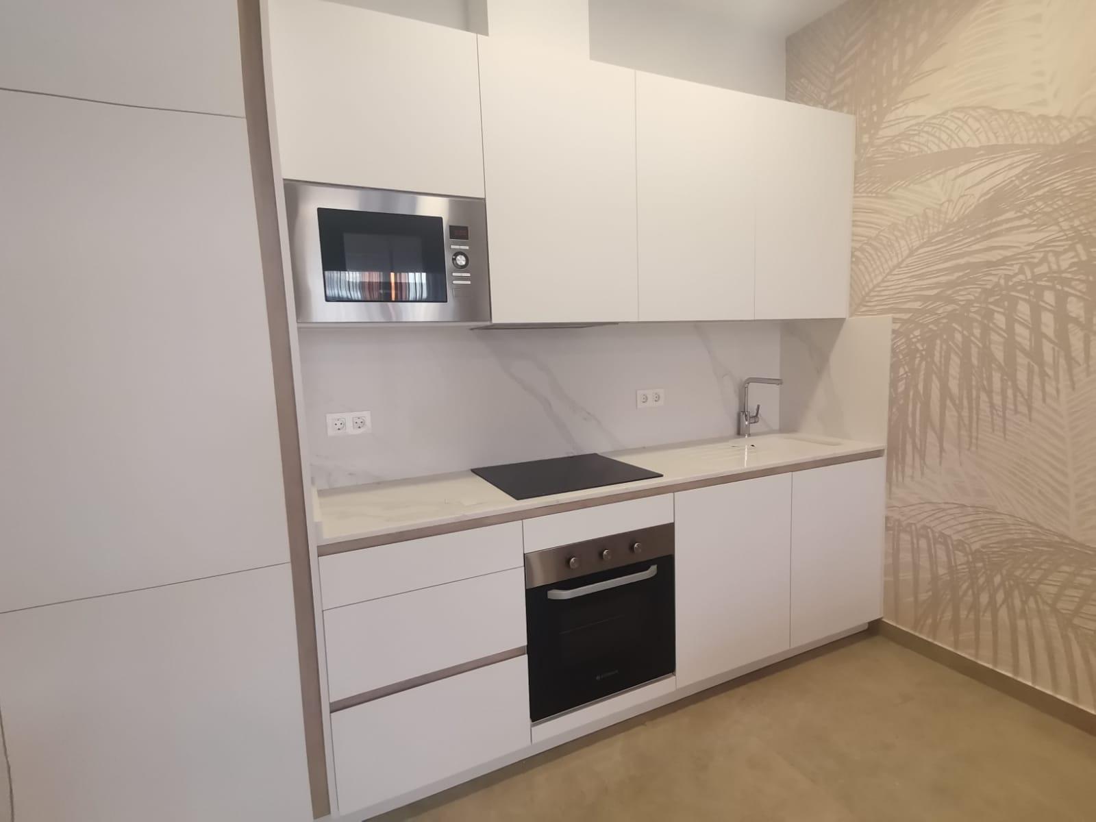 Modern white kitchen with built-in microwave, oven, and induction cooktop, plus a marble backsplash and sink.