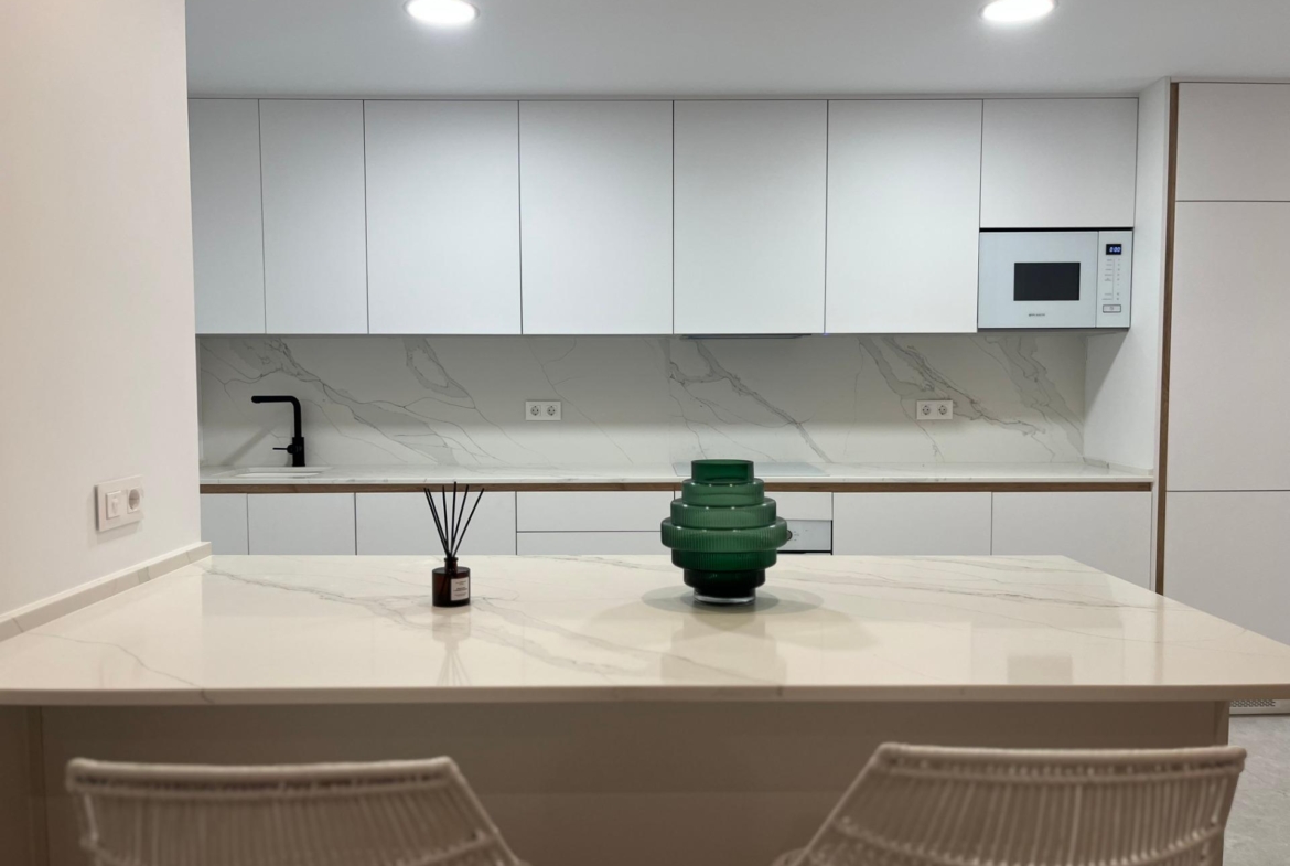 Modern kitchen with white cabinets and marble countertop; island in foreground, green glass tiered centerpiece, and a reed diffuser in a small bottle on the counter