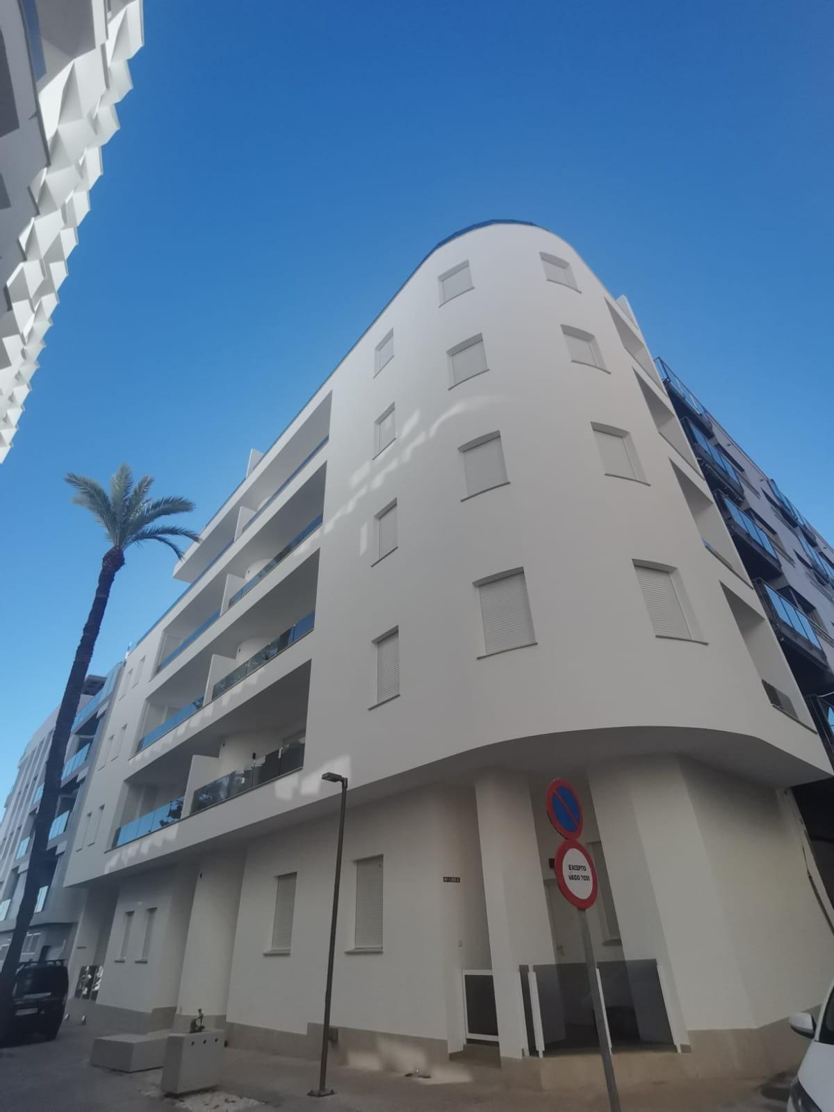 White curved modern apartment building with small windows and balconies set against a bright blue sky, palm tree on the left.