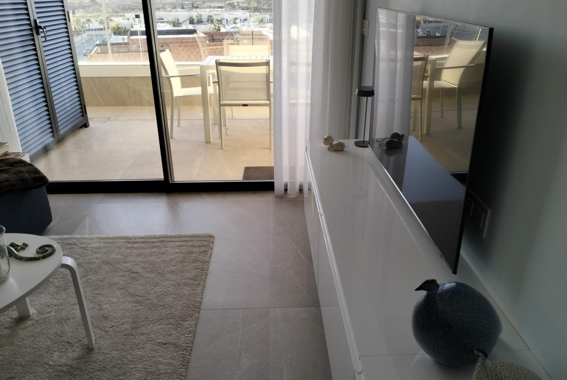 Living room with a balcony view: glass doors, white furniture, and a TV on a white cabinet; outdoor table and chairs on the balcony beyond.