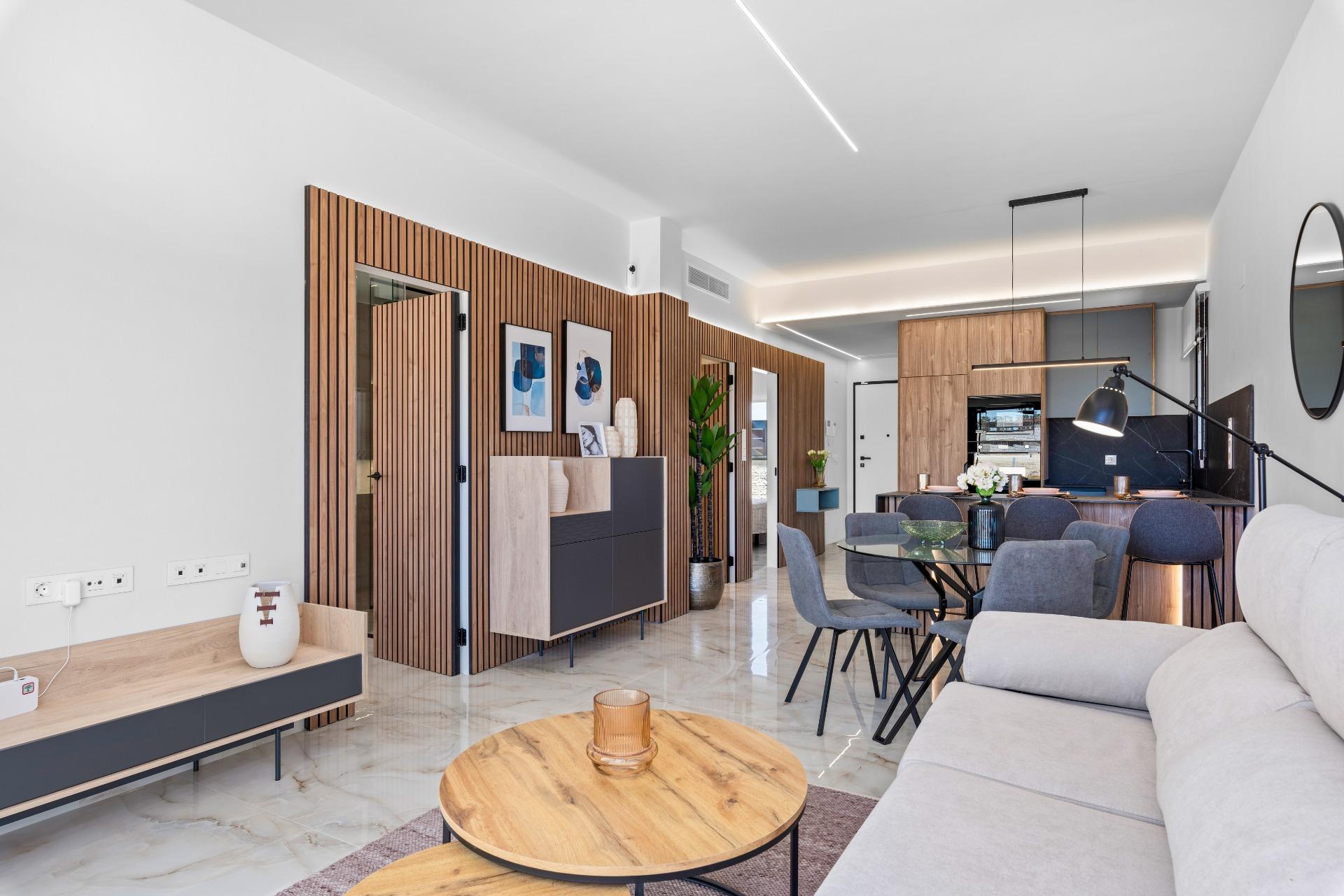 Open-concept living area with wood slat wall, gray sofa, and round wooden coffee table near the dining space