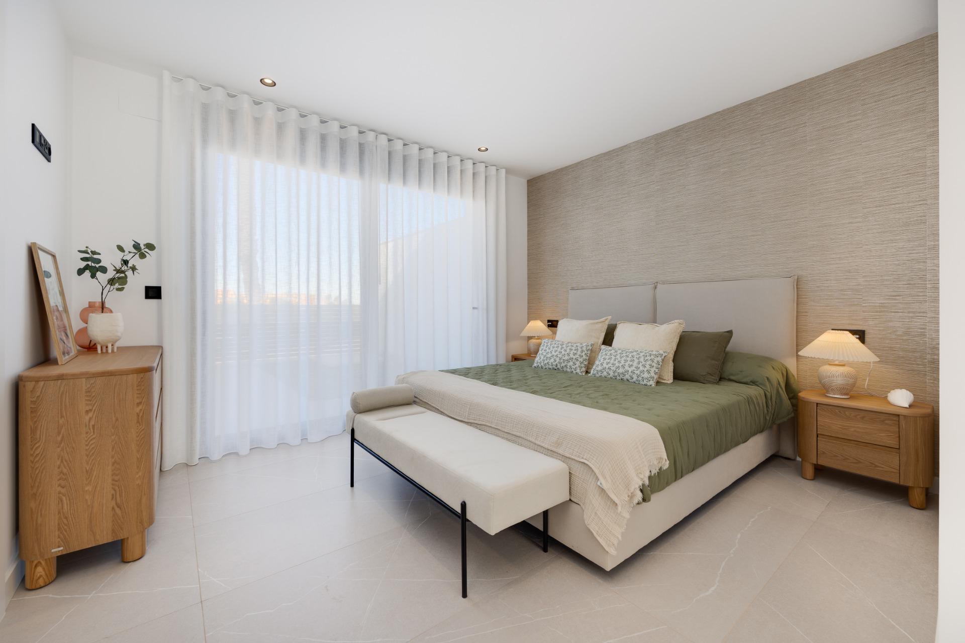 Bright modern bedroom with a low metal-framed bed, olive-green bedding, beige headboard, and wooden nightstands with lamps.