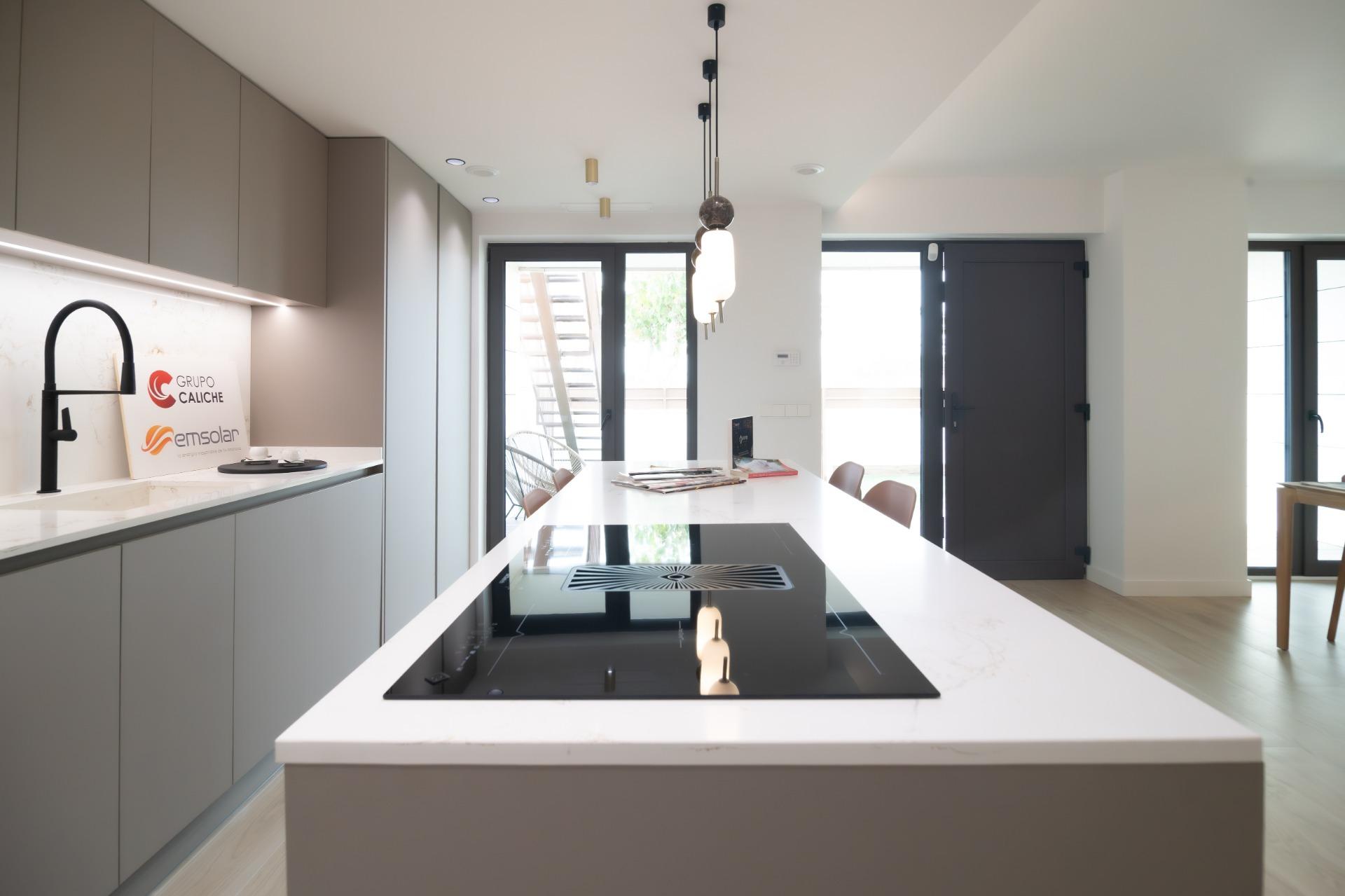 Modern kitchen with a white island, black induction cooktop, and gray cabinets; large glass door at the back leads outside.