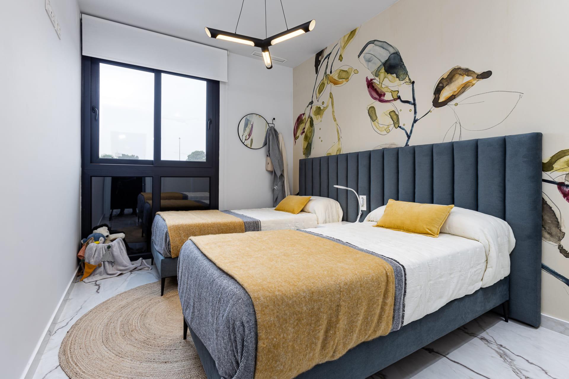 Twin beds in a modern hotel room with blue upholstered headboards, mustard throws, and a colorful botanical mural on the wall.
