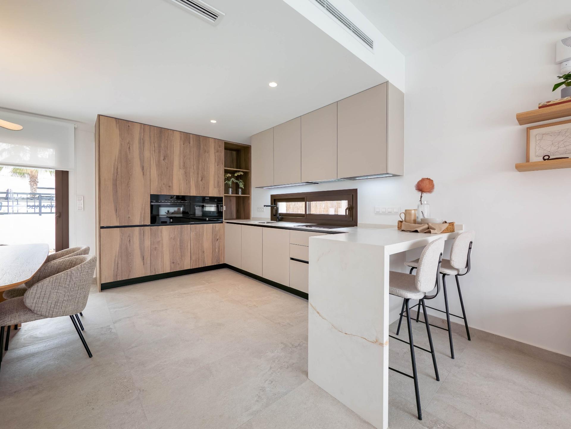 Bright, modern kitchen with wooden tall cabinets, beige upper cabinets, and a white marble island with bar stools.