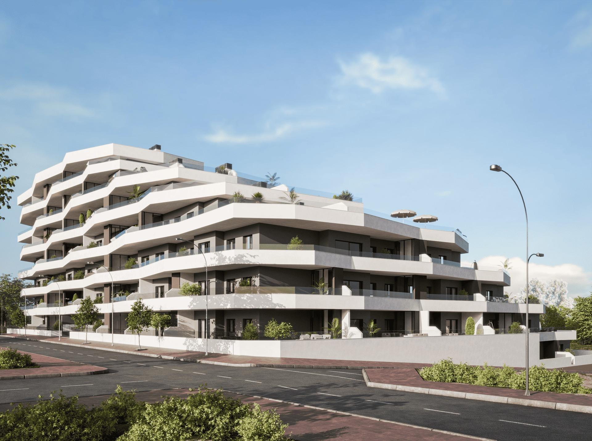 Modern white apartment building with tiered balconies along a curved street edge under a blue sky.