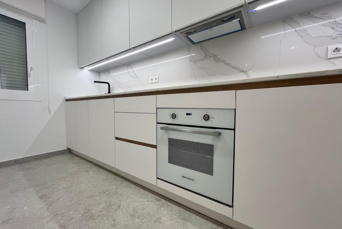 Modern white kitchen with glossy handleless cabinets, built-in oven, marble backsplash, and under-cabinet lighting listia