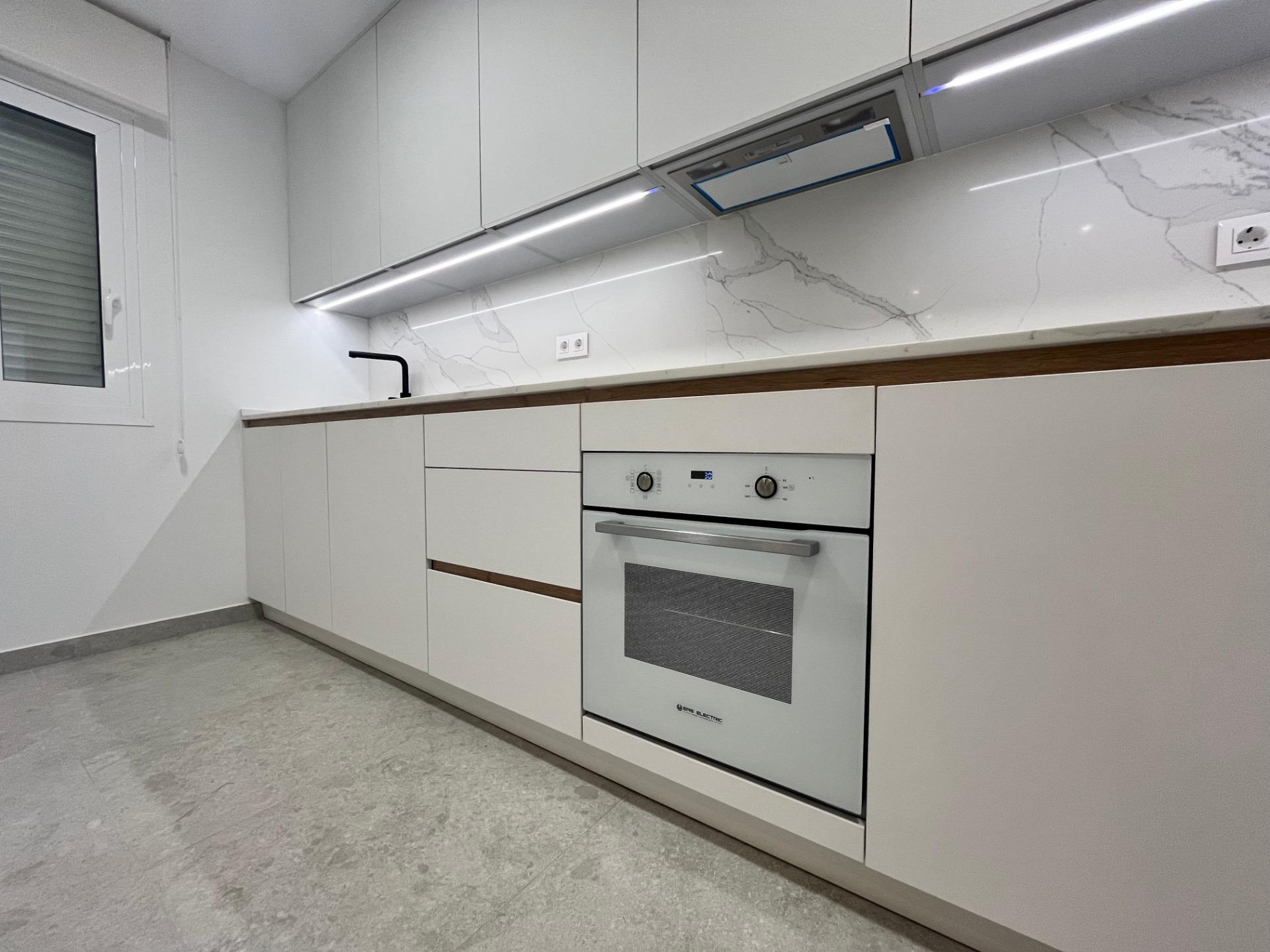 Modern white kitchen with glossy handleless cabinets, built-in oven, marble backsplash, and under-cabinet lighting listia