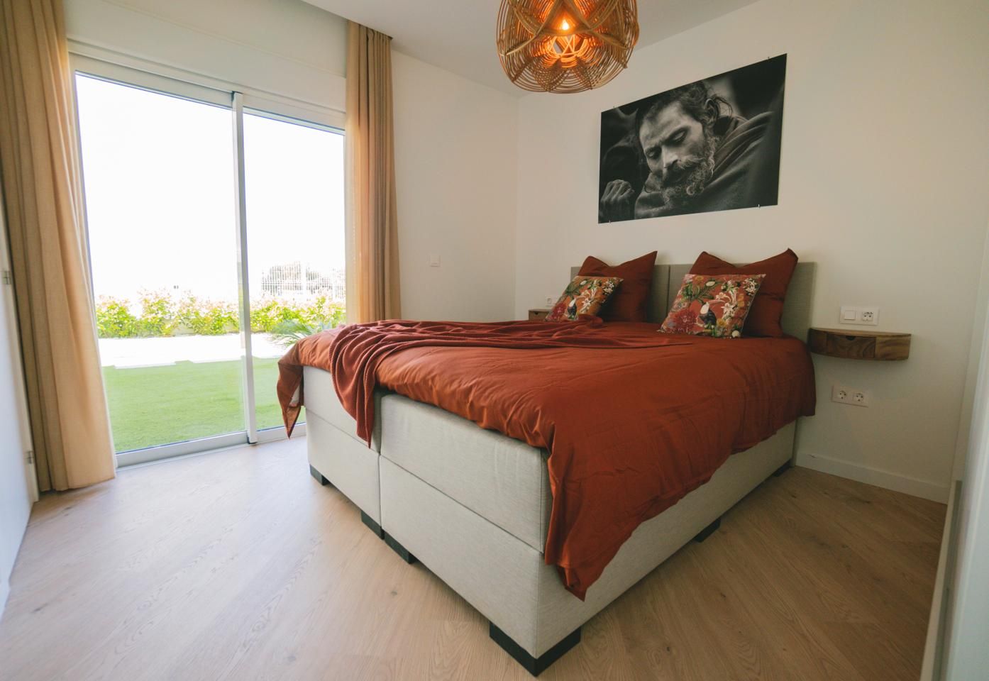 Bedroom with orange duvet and floral pillows on a gray bed, sliding glass doors to a balcony outside across the room.