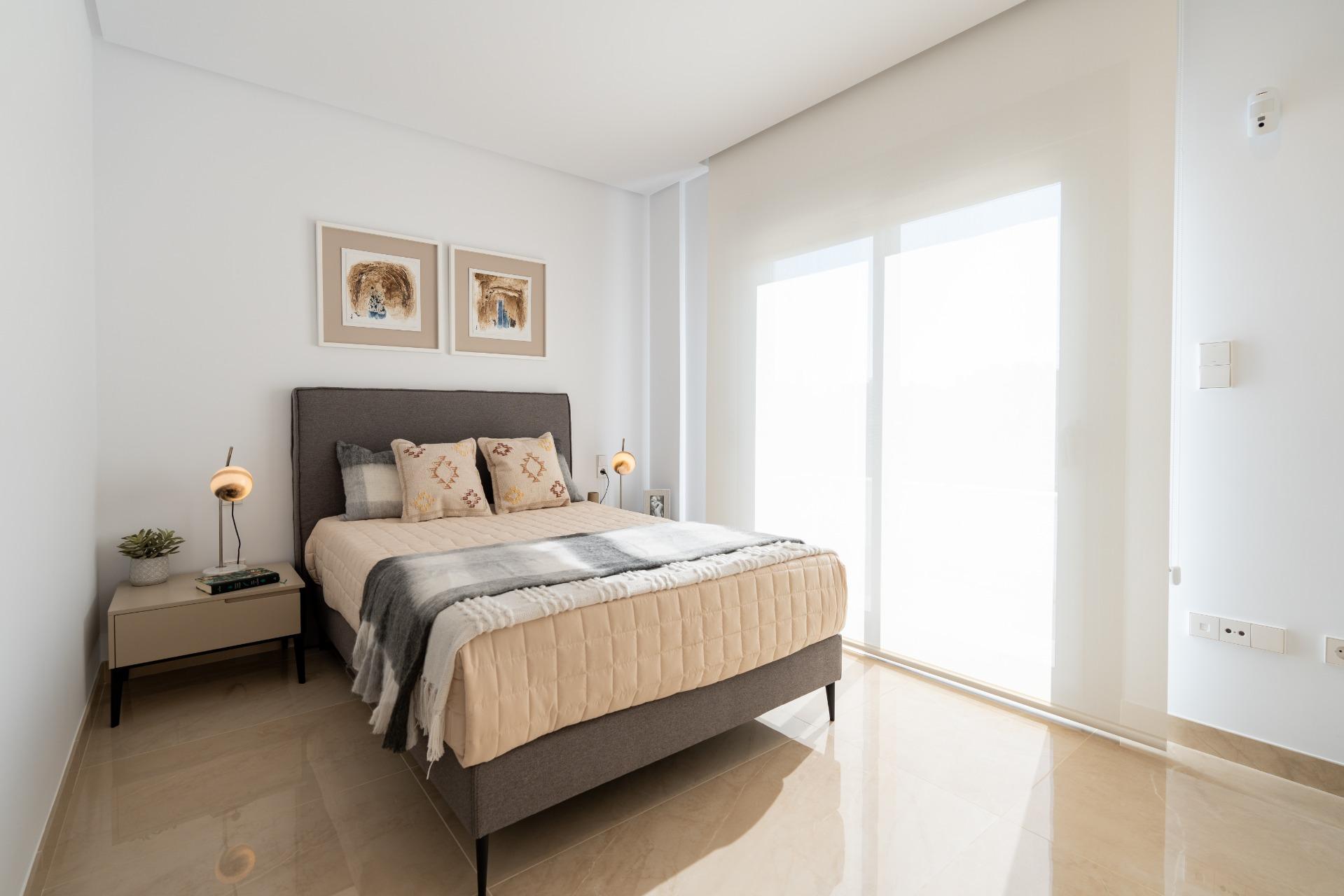 Bright minimalist bedroom with gray upholstered bed, beige quilt, patterned pillows, and two framed artworks above the headboard.