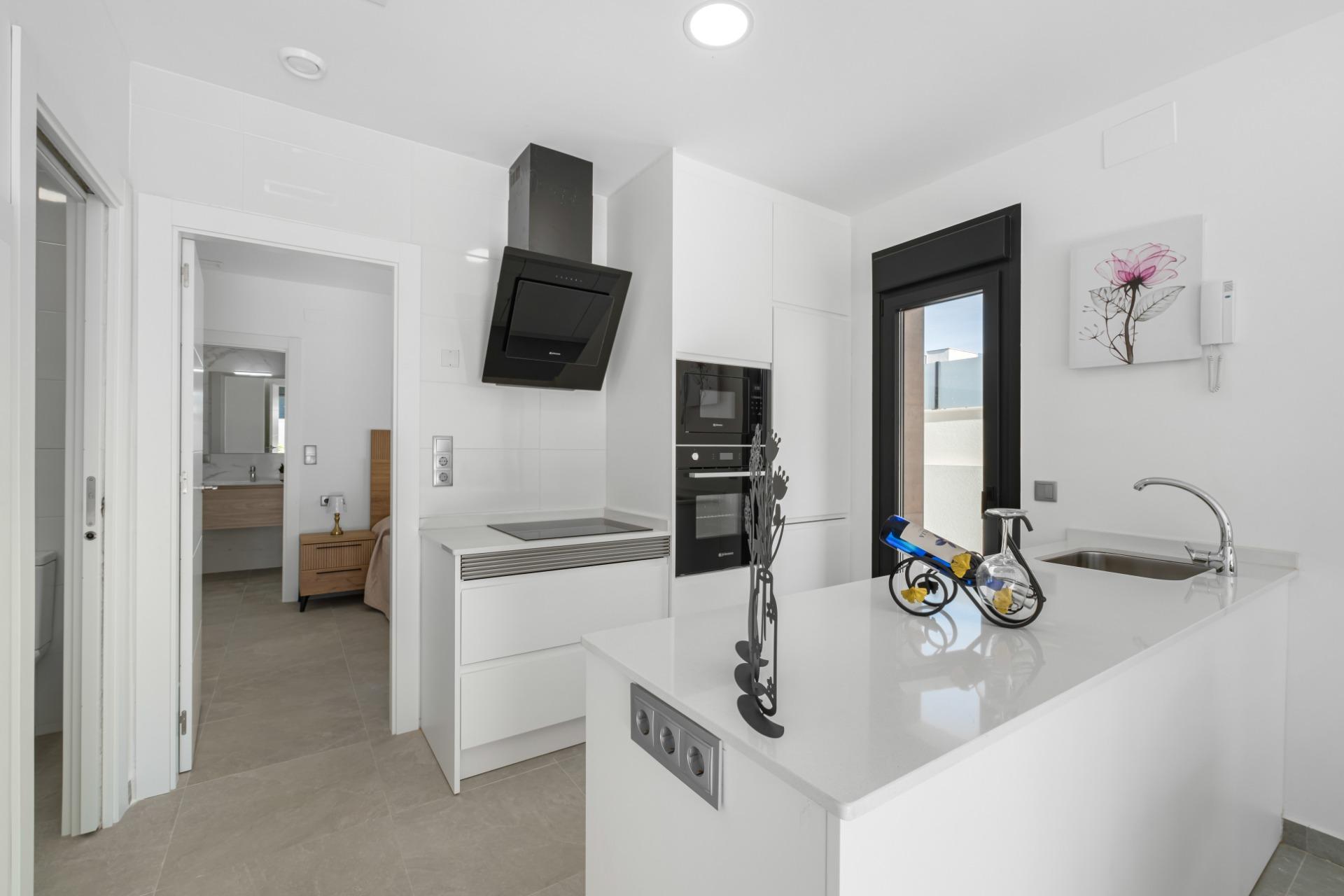 Bright white kitchen with a black angled range hood, built-in oven, white cabinets, and a decorative metal bicycle on the island.