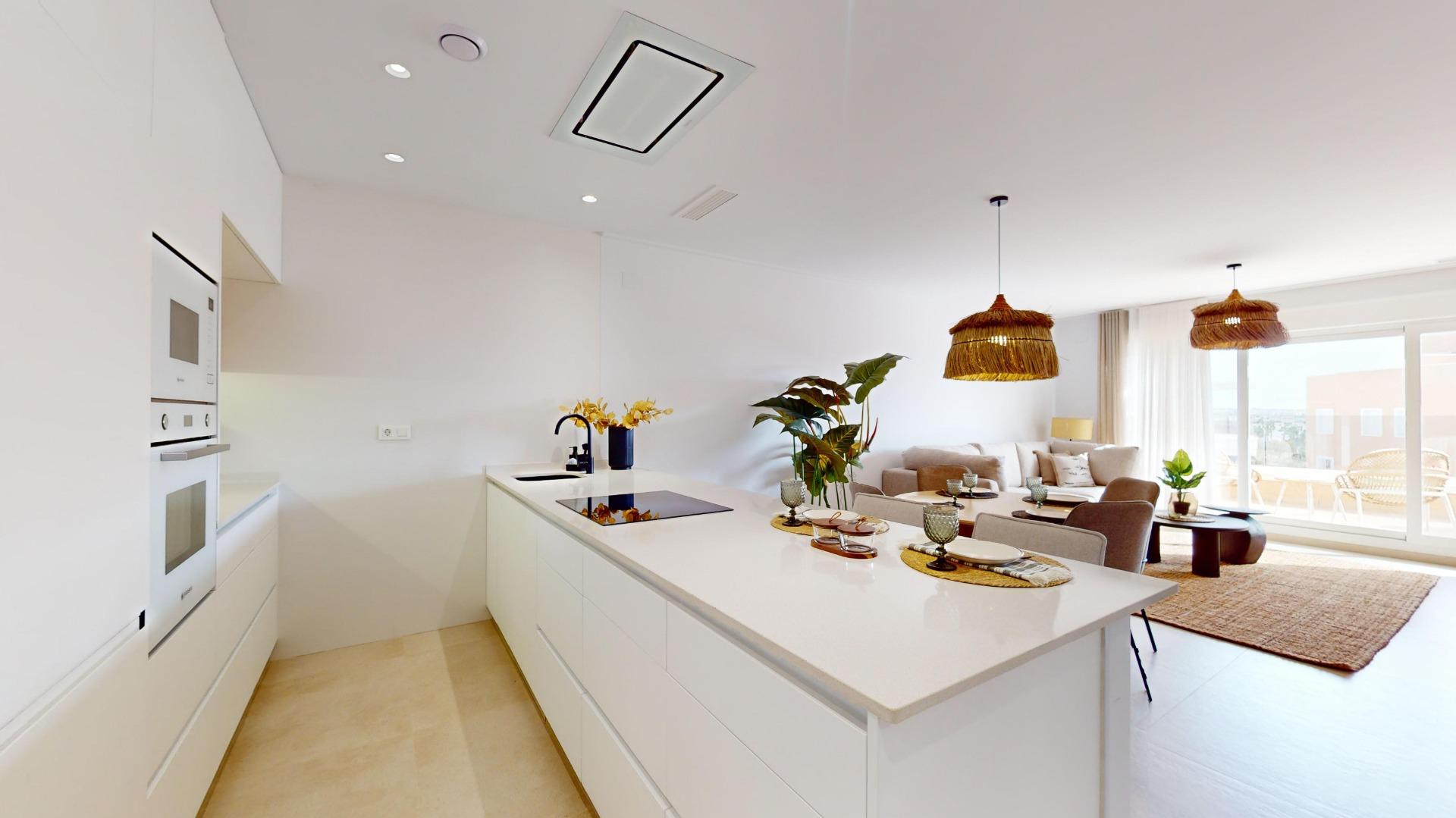 Bright open-plan kitchen with white cabinets and a long island, adjacent living area with wicker pendant lights and a sunny balcony view from sliding doors.