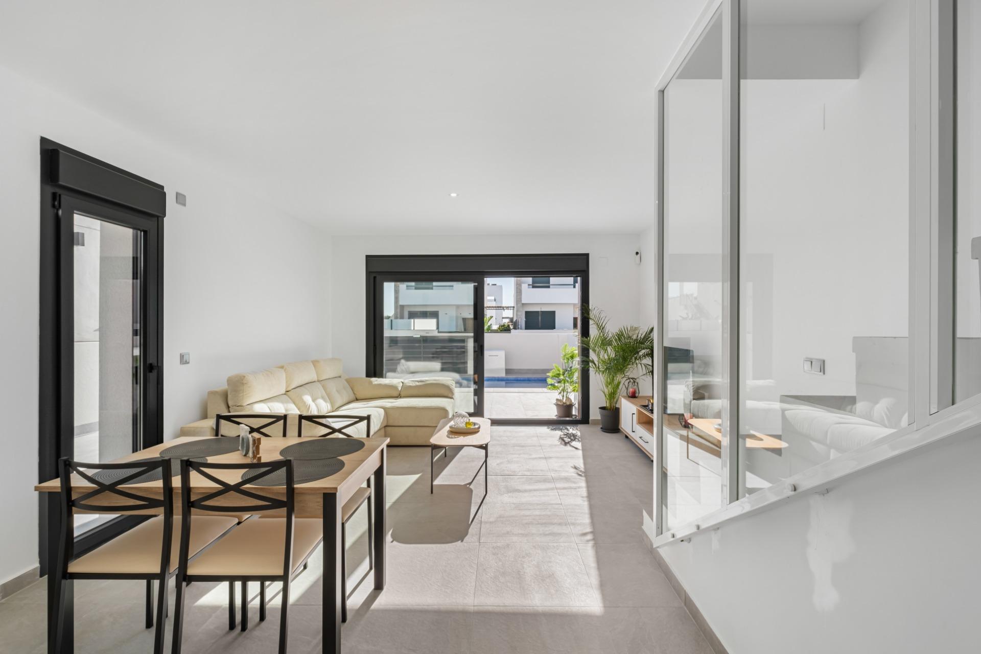 Open-plan living space with a beige sectional sofa, dining table, and glass sliding doors to a sunny patio and pool.