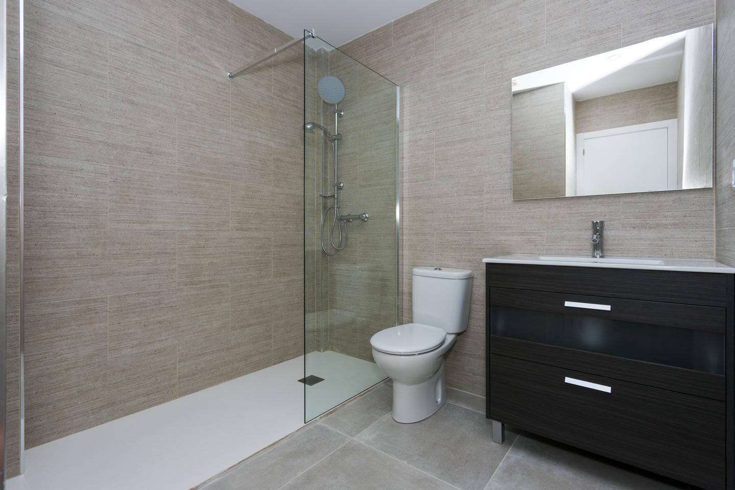 Modern bathroom featuring a glass-enclosed shower, white toilet, dark wood vanity with a white countertop, and a large wall mirror.