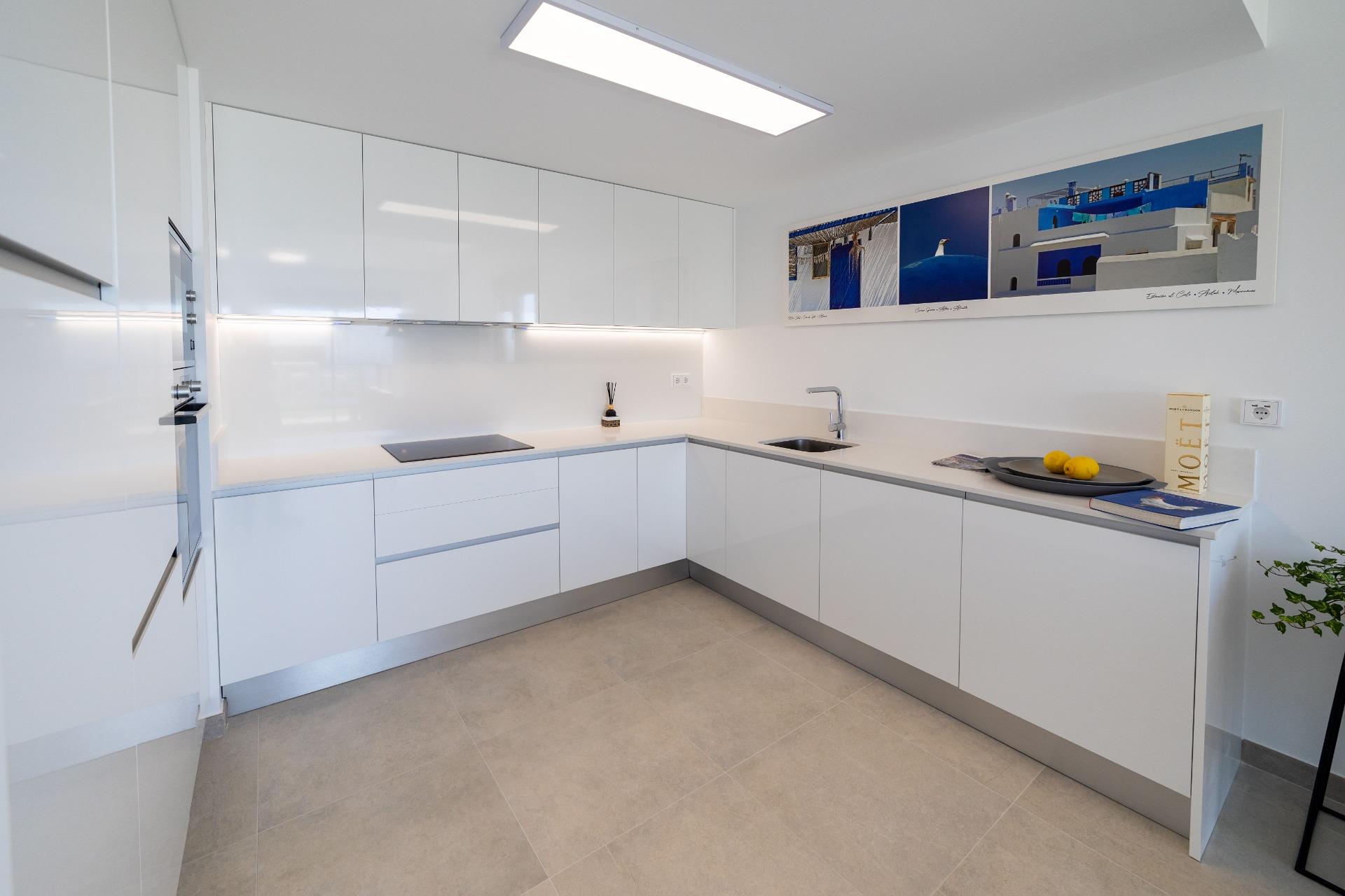 White minimalist U-shaped kitchen with glossy cabinetry, built-in oven, and a sink under bright under-cabinet lighting
