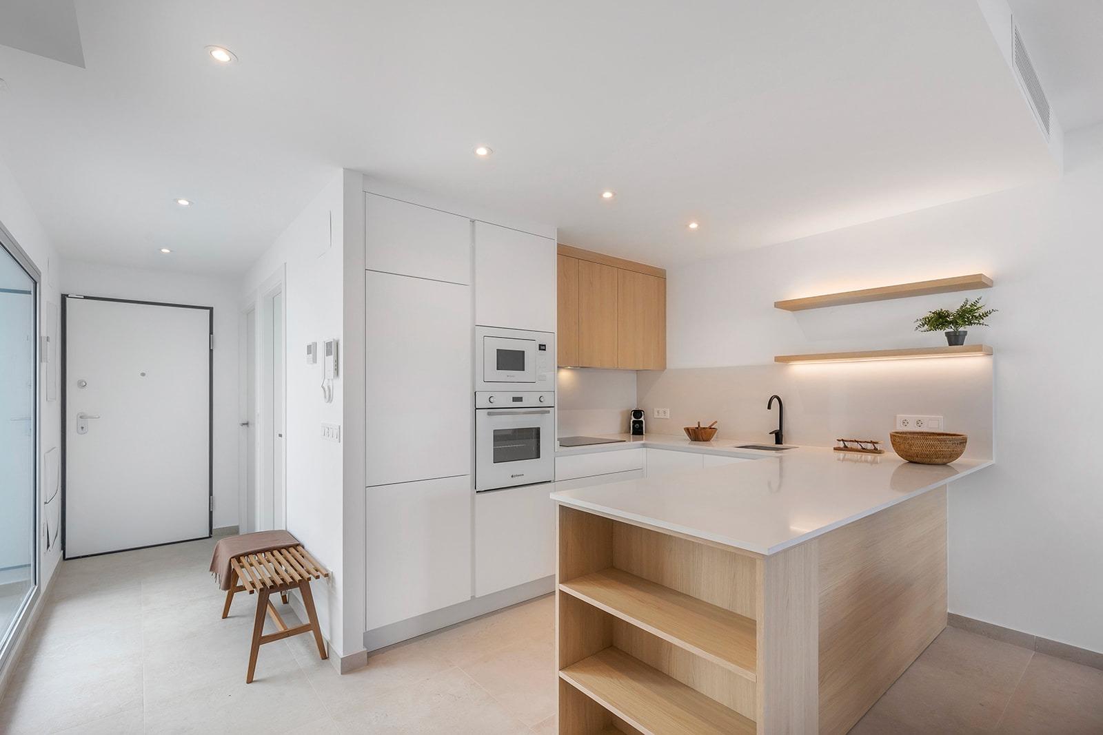 Bright, modern white kitchen with wooden island and open shelves, built-in oven and microwave, and a black faucet over the sink.