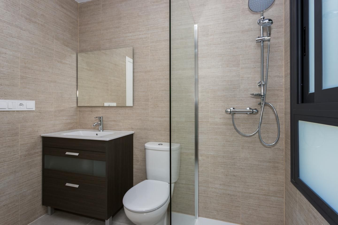 Modern bathroom with a dark wood vanity, white sink, wall mirror, toilet, and glass shower enclosure.