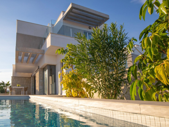 Modern white house with glass balconies by a rectangular pool and lush green trees under a clear blue sky.
