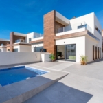 Modern white villa with wooden accents, glass balconies, and a rectangular blue pool in a spacious tiled courtyard