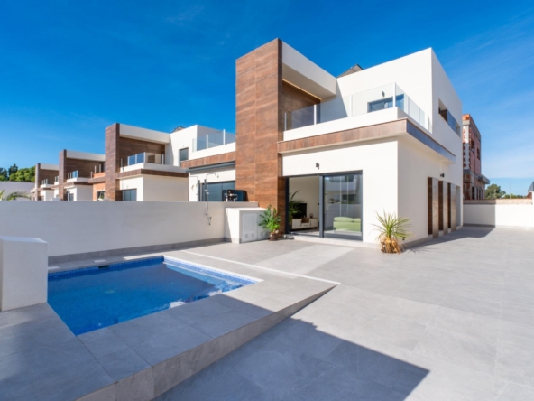Modern white villa with wooden accents, glass balconies, and a rectangular blue pool in a spacious tiled courtyard