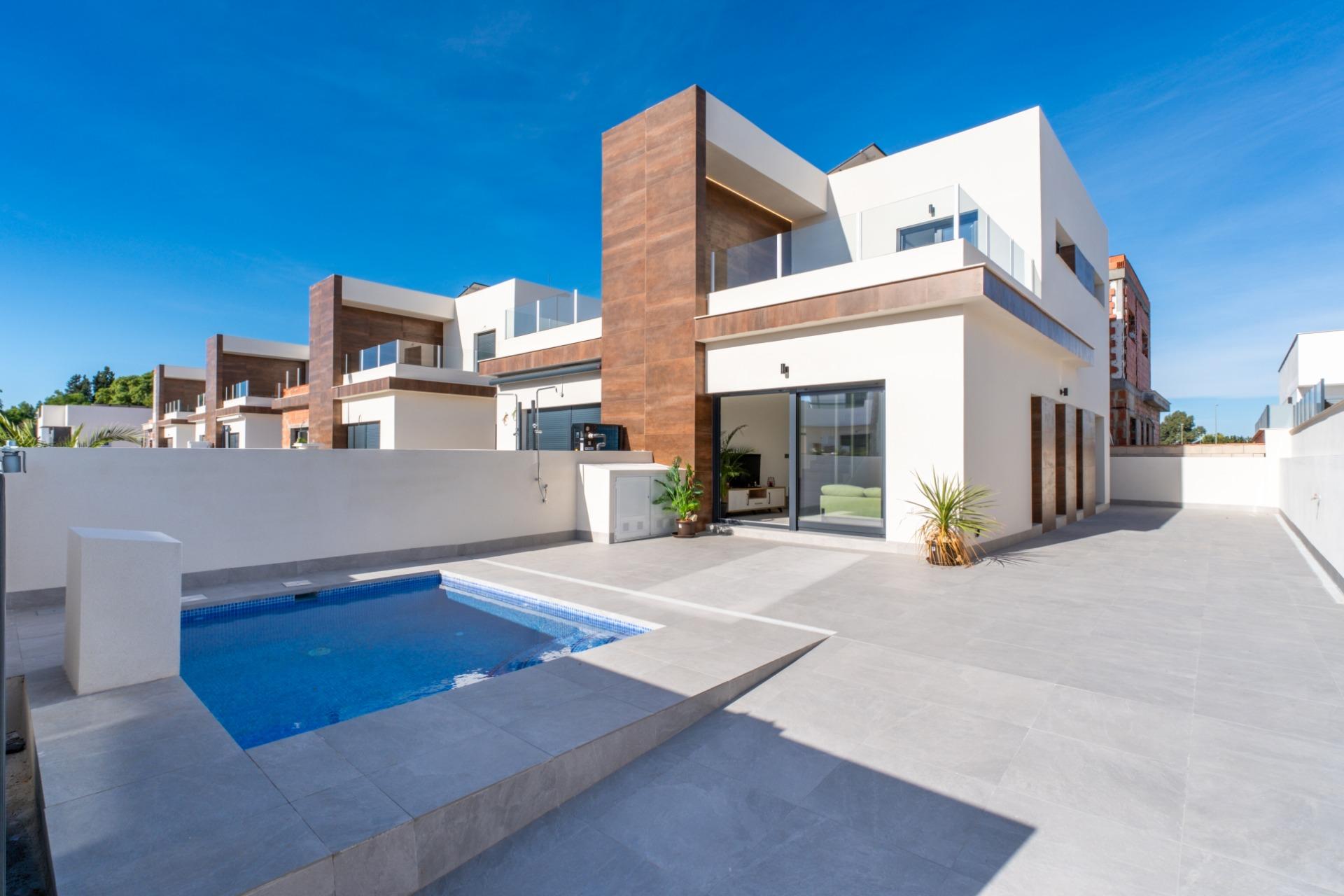 Modern white villa with wooden accents, glass balconies, and a rectangular blue pool in a spacious tiled courtyard
