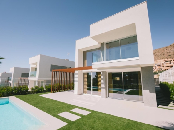 Modern white two-story villa with glass doors, a wooden pergola, and a rectangular pool in a sunny yard.