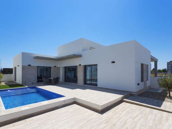 Modern white villa with a rectangular blue pool, glass doors, and a sunlit tiled patio.