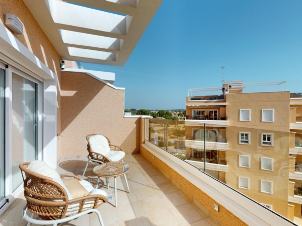 Balcony with wicker chairs and glass table overlooking beige apartment buildings on a clear blue day.