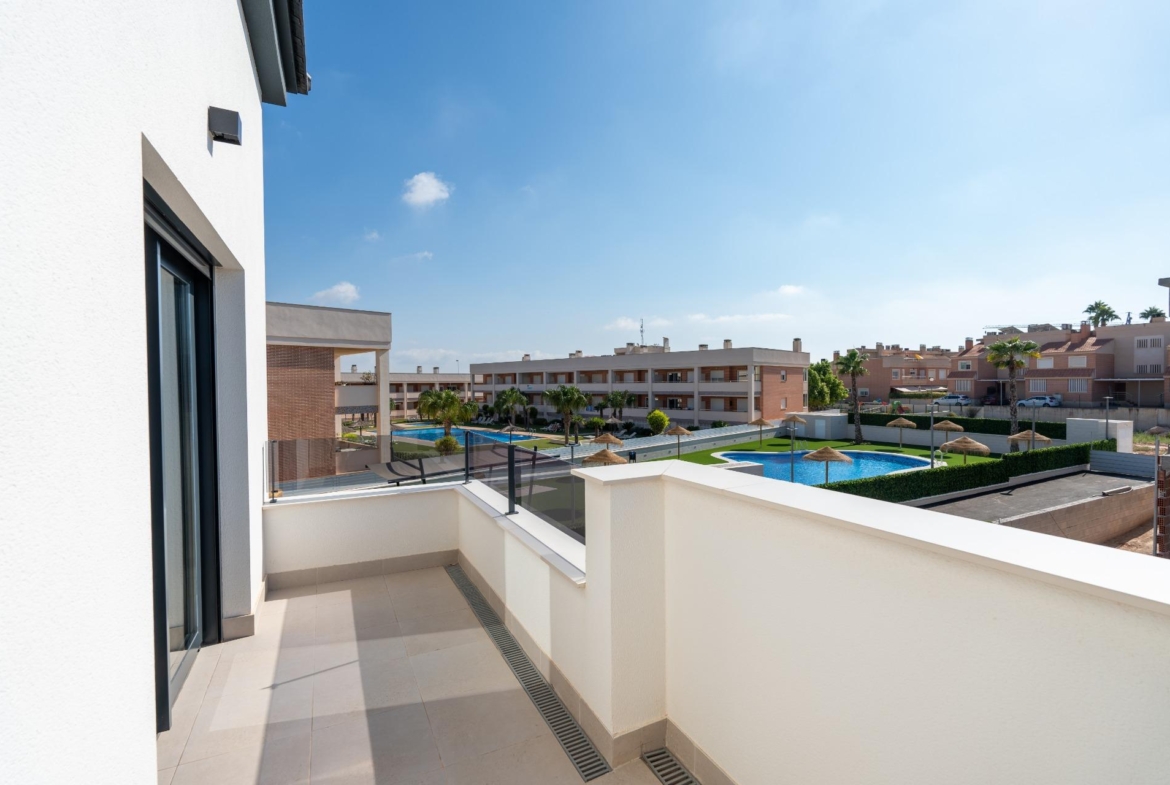 Balcony of a modern white building overlooking a residential complex with a swimming pool and palm trees under a clear blue sky.