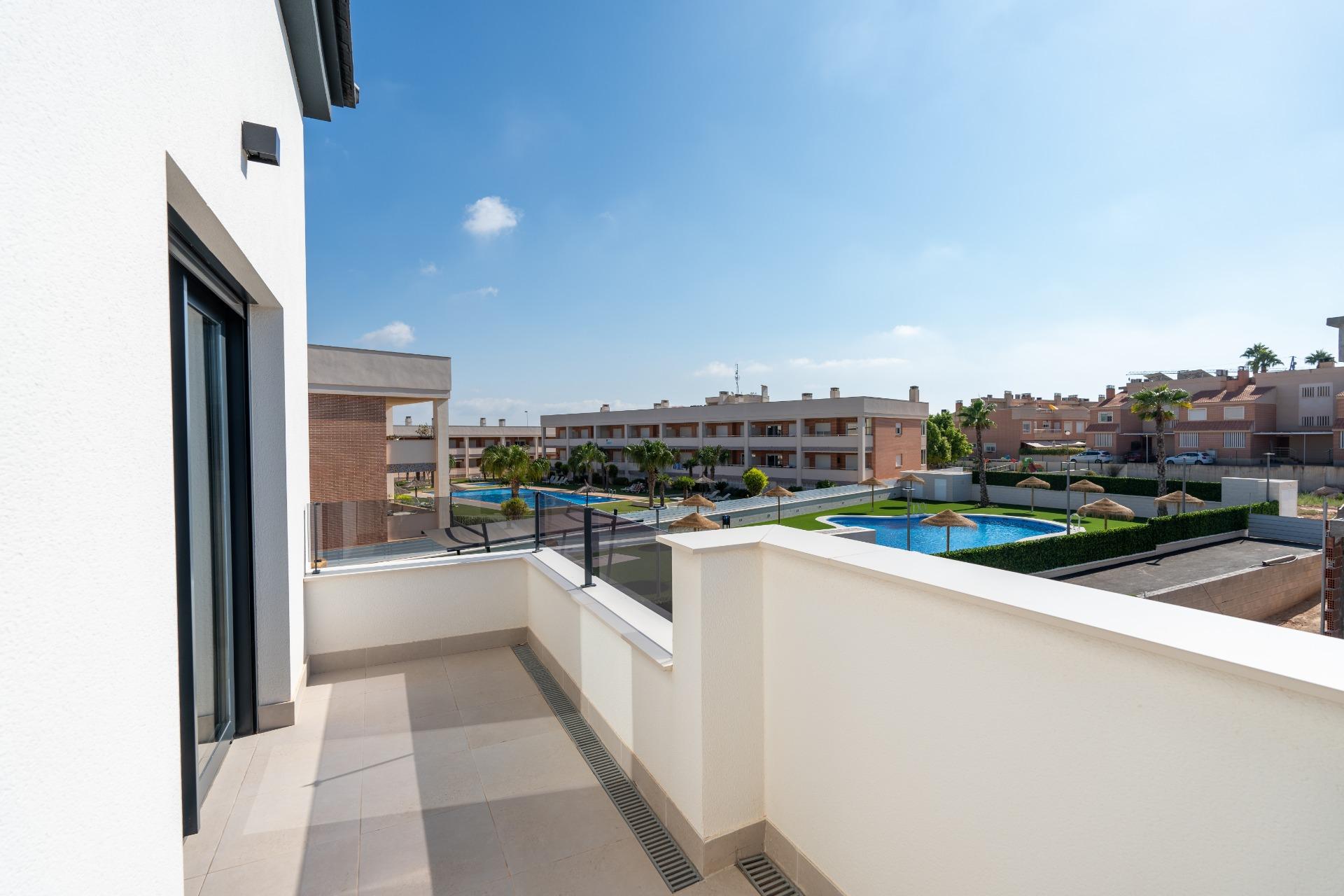 Balcony of a modern white building overlooking a residential complex with a swimming pool and palm trees under a clear blue sky.
