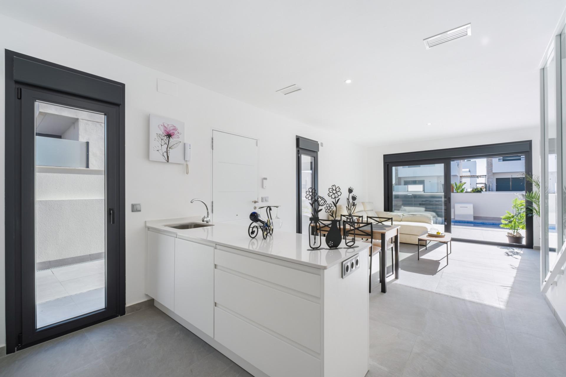 Bright, modern kitchen with white cabinetry and an island, opening to a patio and pool through large glass doors on the right side.
