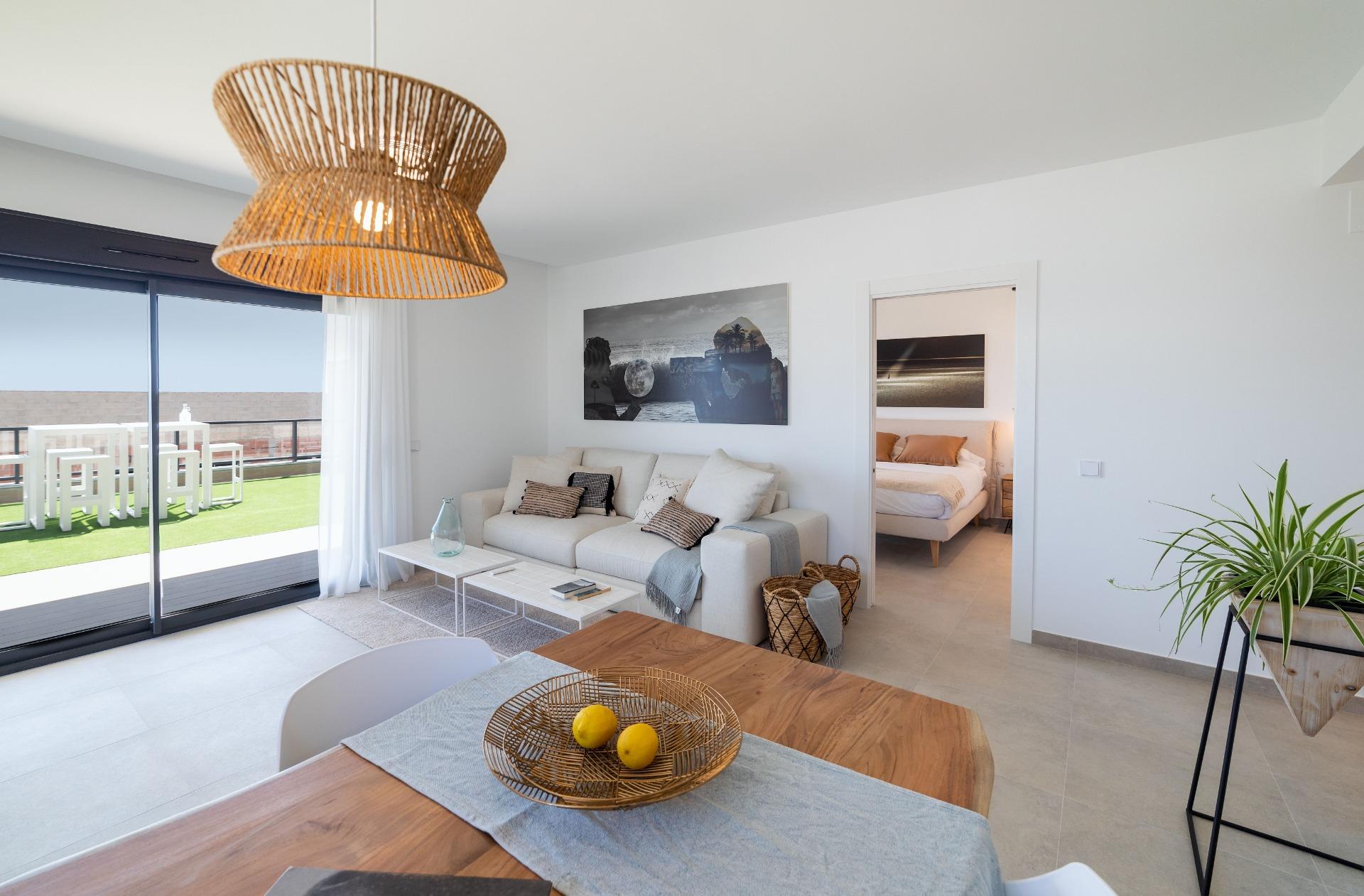 Bright living room with white walls, beige sofa and a wicker pendant lamp; sliding glass doors open to a balcony on the left.