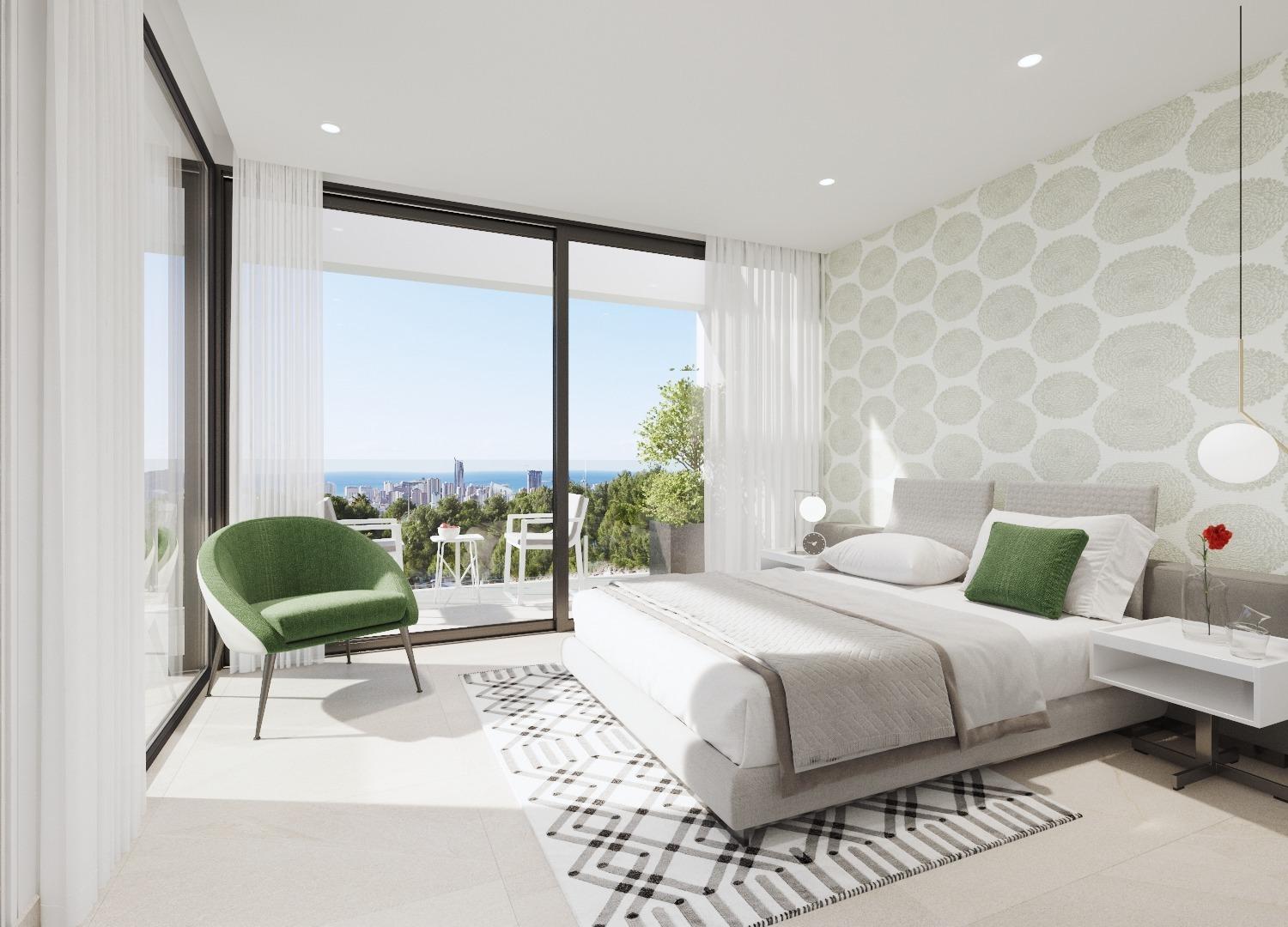 Modern bedroom with a king bed, white bedding and green pillows, patterned feature wall, and a green armchair by tall glass doors opening to a balcony with an ocean view.