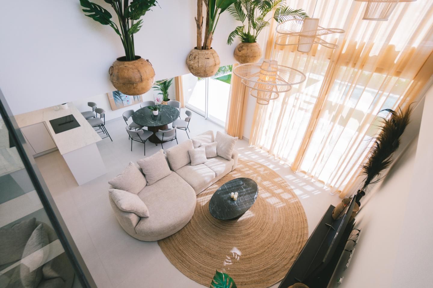 Open-concept living room with beige sectional sofa, round marble coffee table, and a large jute rug by tall windows with sheer curtains