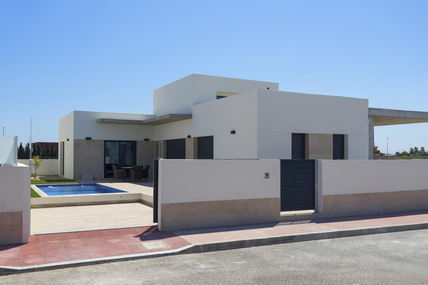 Modern white villa with flat roofs, gated yard, and rectangular in-ground pool beside a paved patio.