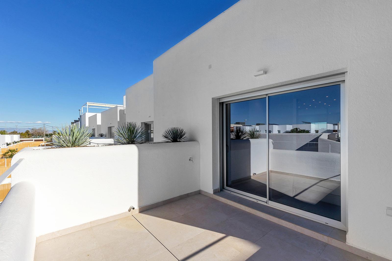 White modern terrace with sliding glass door and potted agave plants under a bright blue sky, desert-inspired landscaping.